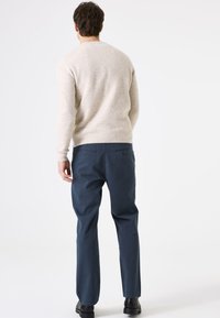 Beige, gemêleerd sweater met lange mouwen, gecombineerd met donkerblauwe broeken. De broeken hebben twee achterzakken en een rechte pasvorm.