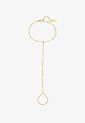 Pulsera de cadena de oro con formas geométricas enlazadas, llevada en un brazo bronceado. La persona que la lleva vestida con una camiseta blanca de canalé, con los brazos cruzados.
