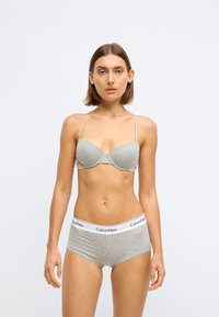 Sutia cinza de algodão com aro e alças finas, combinado com cuecas hipster de algodão cinza com uma faixa de cintura branca com o logótipo da Calvin Klein.