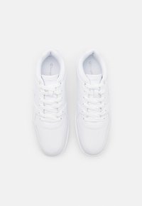 Białe sportowe buty wykonane z gładkiego materiału syntetycznego, charakteryzujące się klasycznym niskim krojem oraz sznurowaniem z tonalnymi akcentami.