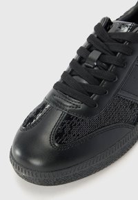Sneaker nera con punta in pelle e pannelli laterali in paillettes nere texture. Design con lacci, suola in gomma e un motivo di aderenza sottile.
