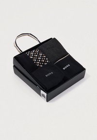 Σετ δώρου με ανδρικές κάλτσες σε μαύρη συσκευασία. Περιλαμβάνει τρία ζευγάρια: ένα ενιαίο μαύρο, ένα σκούρο γκρι και ένα ζευγάρι με σχέδιο τετραγώνων σε χρυσό, λευκό και μαύρο.