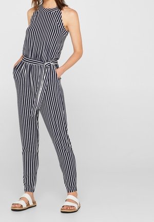 Pasiasty kombinezon z wysokim dekoltem, dopasowaną talią i szerokimi nogawkami. Kolory granatowy i biały z paskiem w talii. Noszony z płaskimi sandałami.