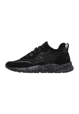 Schwarzer Low-Top-Sneaker mit gemischten Materialien, dicker Sohle mit schwachem Schriftzug, vorderer Schnürung und samtigem Futter sichtbar am Knöchelkragen.