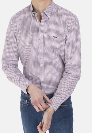 Man past de manchet aan van een lange mouwen, geruit, met knopen sluitend overhemd met een klein hondenlogo, draagt blauwe spijkerbroek tegen een effen achtergrond.
