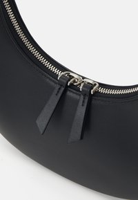 Svart lærveske med halvmåneform, med sølvfarget glidelås og to teksturerte glidelåsstropper. Glatt overflate med minimale detaljer.