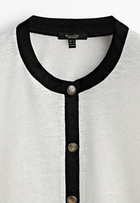 Tissu blanc avec col rond noir et patte de boutonnage comportant trois boutons décoratifs argentés.