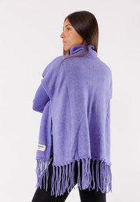 Poncho lavorato a maglia viola con colletto alto, caratterizzato da bordi frangiati e un'etichetta sull'orlo. Tessuto morbido e vestibilità comoda.