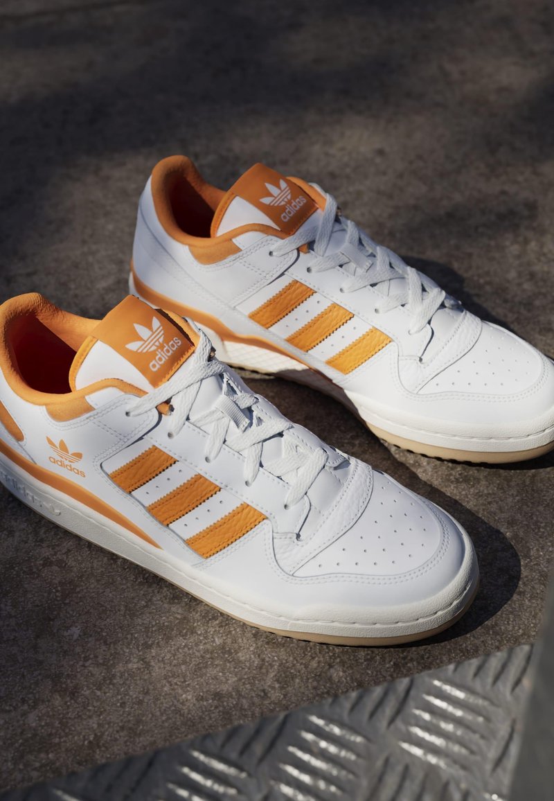 Vita lädersneakers med orange accenter. Har tre orange ränder, perforerad tå och en vadderad krage. Gummisula med texturerat grepp.