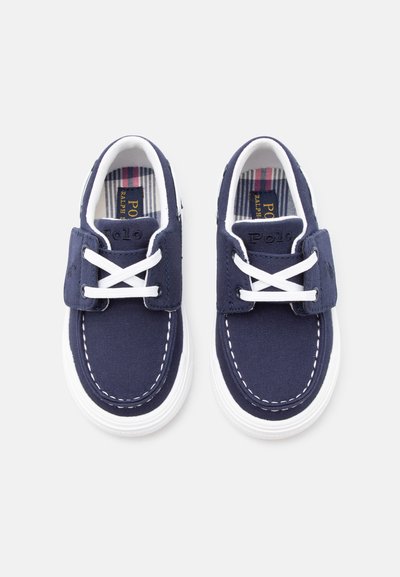 Παιδικά ναυτικά παπούτσια σε σκούρο μπλε χρώμα με λευκές σόλες, λευκά κορδόνια και καρό εσωτερική επένδυση, με λογότυπο "Polo" στη γλώσσα και στις πλευρές.
