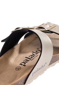 Sandalia deslizante negra y plateada con una plantilla texturizada, correas ajustables con hebilla dorada y suela de corcho. El nombre de la marca "palado" es visible.