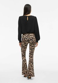 Zwarte top met lange mouwen en een open rugdetail, gecombineerd met bruine wijde broek met luipaardprint, die textuur en aparte patronen accentueert.