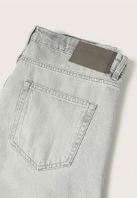 Jeans in denim grigio chiaro con una tasca posteriore e una toppa in pelle marrone testurizzata in vita, con dettagli di cucitura standard.