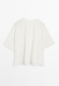 T-shirt blanc surdimensionné à manches courtes avec un col rond simple et un détail de couture au dos, présenté sur un fond blanc uni.