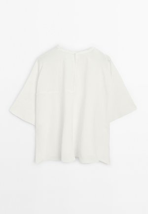 T-shirt blanc surdimensionné à manches courtes avec un col rond simple et un détail de couture au dos, présenté sur un fond blanc uni.
