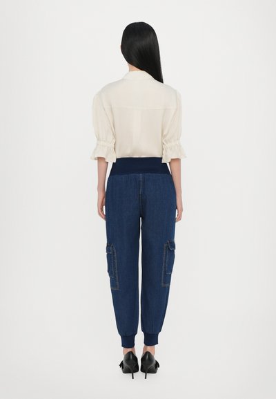 Cream, puff-sleeved blouse with ruched detailing; paired with navy denim jogger pants featuring side pockets and ribbed cuffs. Black heels shown.