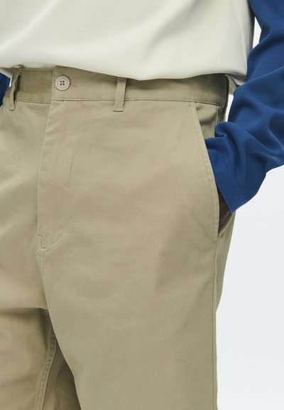 Pantalon en coton beige à coupe droite, avec une fermeture à bouton et des poches latérales, assorti à un haut bleu à manches longues.