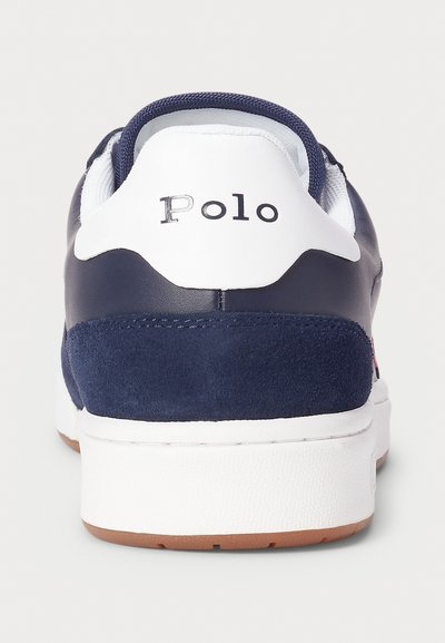 Navy blue sneaker featuring a white sole, suede detailing, and a heel tab with "Polo" logo in silver. Breathable mesh tongue.