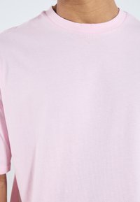 Lyserosa bomulls T-skjorte med rund hals og korte ermer, med en glatt tekstur og et enkelt, uformet design.
