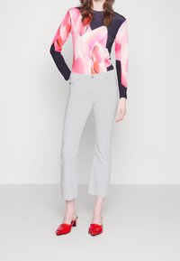 Pitkähihainen paita, jossa on vaaleanpunainen ja tummansininen abstrakti kuvio, yhdistettynä vaaleanharmaisiin housuihin ja punaisiin avojalkaisiin korkokenkiin.