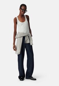 Witte tanktop, gestreepte shirt geknoopt om de taille, donkerblauwe wijde jeans en zwarte schoenen met een gestructureerd patroon. Bril maakt de look af.