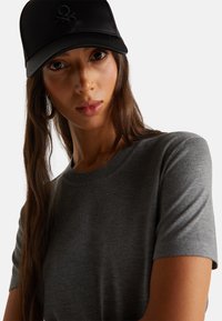 Šedé pletené tričko s krátkými rukávy, v kombinaci s černou čepicí s vyšitým logem. Hladká textura s přiléhavým střihem.