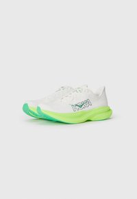 Baskets blanches de sport avec des accents verts et une semelle texturée, présentant un logo "HOKA" en évidence et un design moderne et épuré.