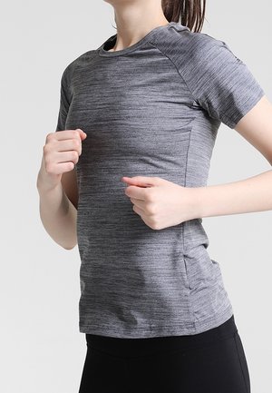 Kvinde iført en grå kortærmet sportsbluse og sorte leggings, der jogger eller løber mod en ensartet lys baggrund.