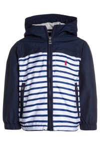 Námořnicko-modrý pruhovaný kabát s kapucí, vybavený zipem vpředu a dvěma bočními kapsami. Materiál vypadá lehký a hladký. Červený logotyp jako detail.