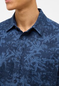 Camicia blu navy abbottonata con un motivo testurizzato di foglie blu più chiare, dotata di taschino e design del colletto classico.