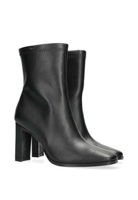 Botas de tobillo de cuero negro con punta afilada, tacón bloque apilado y detalles de costura mínimos. Textura suave y diseño elegante.