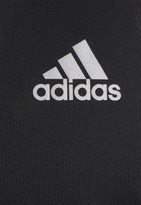 Tessuto sportivo nero con una superficie texturizzata, caratterizzato da un prominente logo Adidas bianco e il dettaglio delle tre strisce.