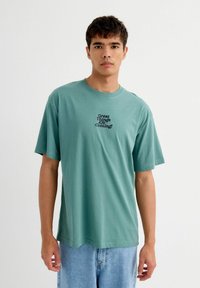 camiseta de algodón color verde menta con cuello redondo y mangas cortas. Presenta un texto en negro que dice "¡Grandes cosas están por venir!" en la parte frontal.