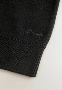 Crna pletena majica s rebrastom teksturom i izvezenim "Clarks" logom na donjem lijevom dijelu. Jednostavan dizajn s okruglim izrezom i dugim rukavima.