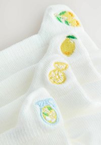 Tissu blanc avec des motifs brodés sur le thème du citron, comprenant un citron, des tranches de citron et une carafe de limonade avec des glaçons et des feuilles.