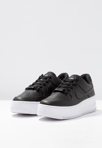 Pair of black Nike Air Force 1 sneakers with white soles, black laces, and Nike swoosh logo on the sides, set against a plain white background.