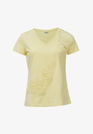 Camiseta de algodón amarilla con escote en V, que presenta un detalle de encaje a lo largo de un hombro y bajando por un lado, creando un contraste texturizado.