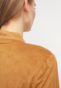 Kortärmad skjorta i senapsfärgad mocka med en jämn yta och en mjuk krage, som har diskret puffade axlar och minimal detaljering.