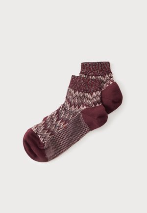 Une paire de socquettes bordeaux avec un motif en maille et des parties unies au niveau des orteils et des talons sur un fond blanc uni.