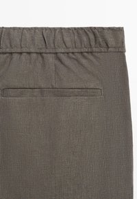 Pantalon en tissu gris foncé avec une ceinture élastique et une unique poche passepoilée horizontale au dos.
