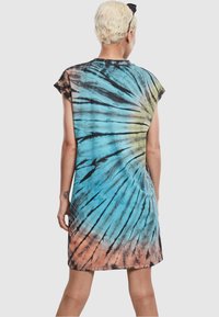 Sukienka w stylu tie-dye z spiralnym wzorem w odcieniach niebieskiego, czarnego i pomarańczowego. Krótkie rękawy i luźny krój z okrągłym dekoltem.