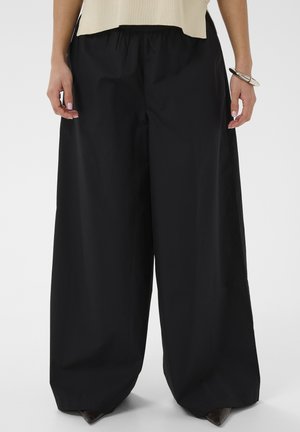 Črne široke hlače z elastiko v pasu, izdelane iz gladkega materiala; imajo čist dizajn in sproščen kroj.