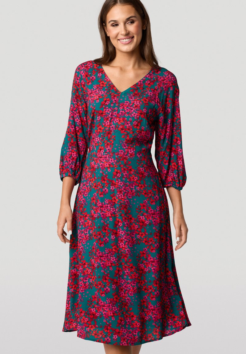 Bloemendress met een teal basis en roze en rode bloemen, V-hals en driekwart puffmouwen. Zachte stof met een vloeiende uitstraling.