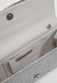 Borsa a tracolla argentata con una morbida interni grigio chiaro. Presenta una chiusura a bottone e una tasca etichettata 'ANNA FIELD'.