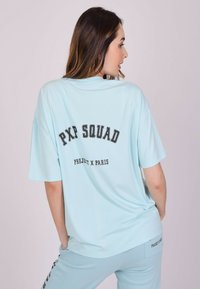 Camiseta de gran tamaño de color azul claro hecha de algodón, con el texto negro "PXP SQUAD" y "PROJECT X PARIS" en la parte posterior. Mangas cortas, cuello redondo.