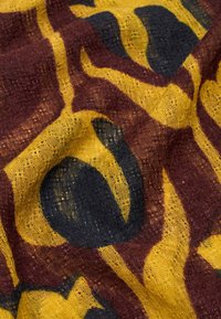 Multicolored fabric with a textured weave. Features a yellow background with dark brown and black abstract patterns. Soft, lightweight material.