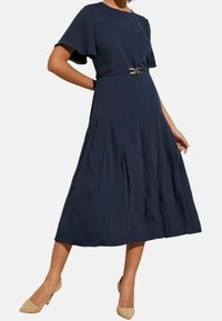 Tyrkysově modré plisované šaty s krátkými volánkovými rukávy a kovovým páskem v pase. Hladký materiál, délka po kolena.