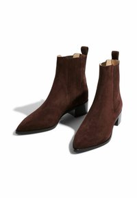Botas de ante marrón hasta el tobillo con puntera afilada, paneles laterales elásticos y lengüetas para facilitar el calzado. Cuentan con un tacón bajo y ancho para mayor estabilidad.