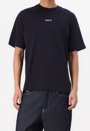 T-shirt en coton bleu marine à manches courtes, avec un logo blanc "REPLAY" centré sur la poitrine. Design simple et coupe décontractée.