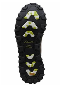 Sole in gomma nera con battistrada aggressivo. Presenta accenti bianchi e verde lime in un motivo a zigzag, con il testo del logo al centro.
